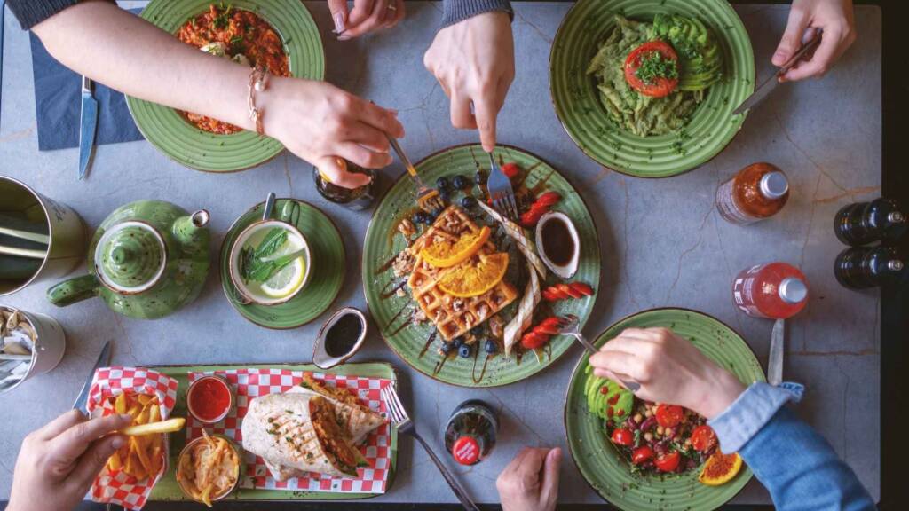 A family enjoys a diverse spread of vegan dishes at Avocado and Coffee, highlighting the cafe's ability to cater to all ages with delicious, nutritious options.